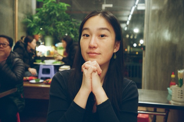 Lily at a restaurant table, chin resting on clasped hands