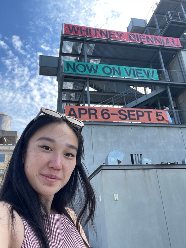 Lily outside the Whitney under Whitney Biennial banners